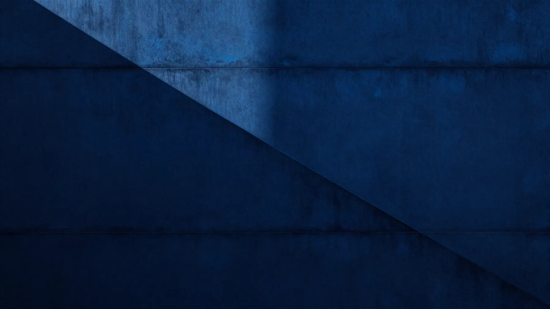 Fachada de hormigón azul oscuro atravesada por un haz de luz