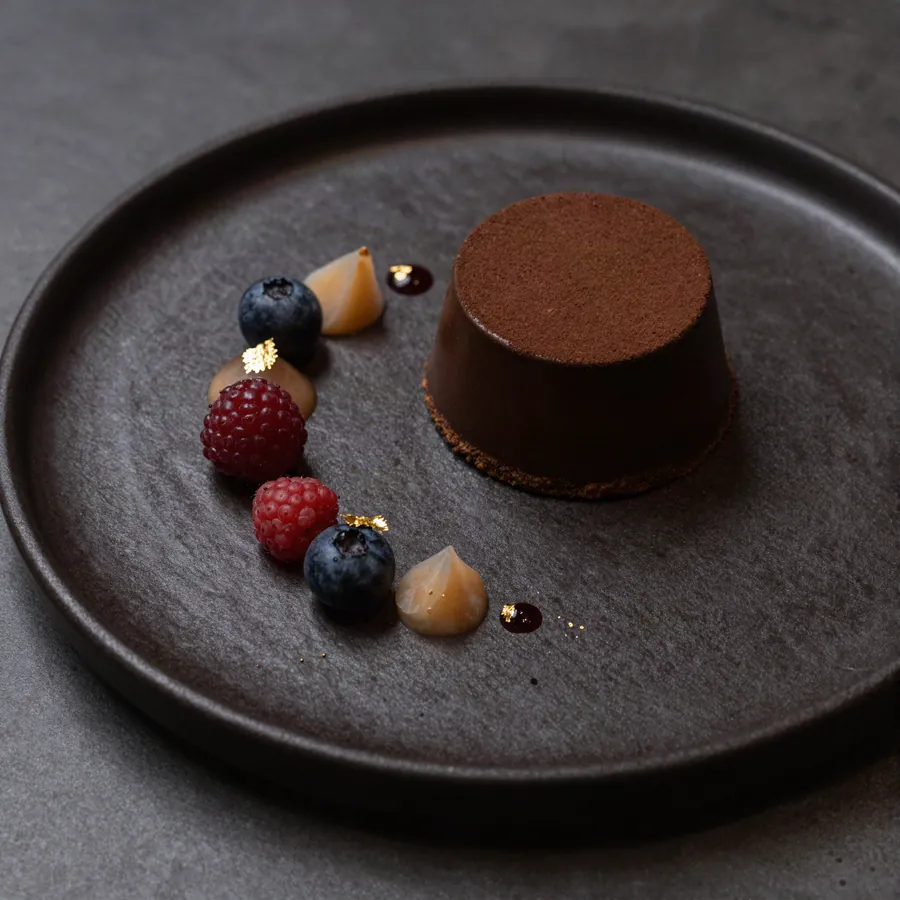Postre de chocolate con frutos rojos sobre plato oscuro